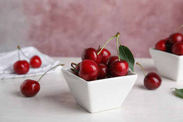 Bowl with ripe sweet cherries on white wooden table