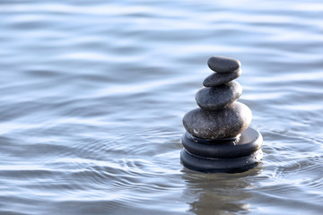 Stack of dark stones in sea water, space for text. Zen concept