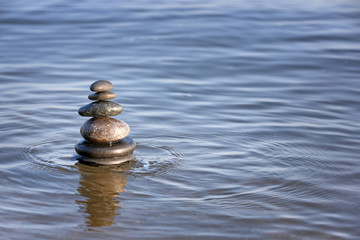 Stack of dark stones in sea water, space for text. Zen concept
