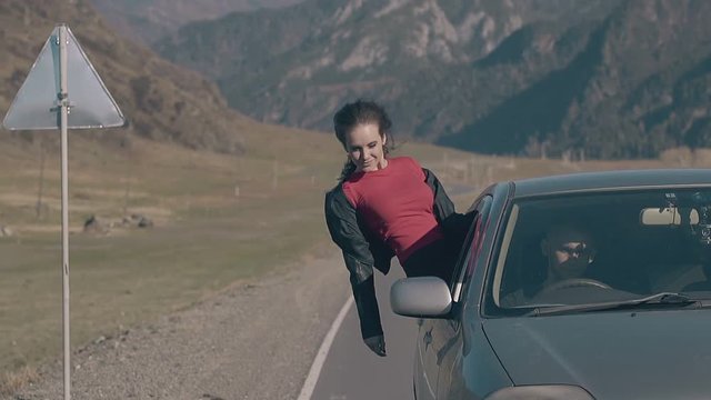happy woman in leather jacket looks down with extended arms screams with happiness in driving car close view slow motion