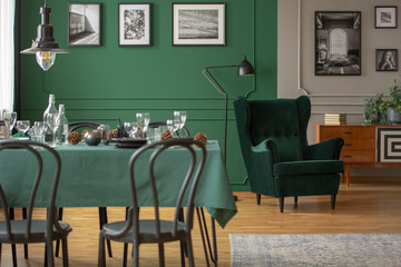 Real photo of a table with green cloth and black chairs in blurred foreground and a comfy armchair in the background in dining room interior