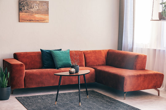 Elegant small wooden coffee table with lowers in front of big velvet corner sofa with pillows