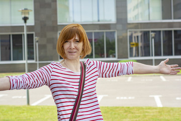 Obraz premium Red-haired, informally-dressed middle-aged woman with freckles stands with her arms wide open