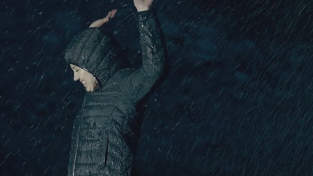 happy lady in green jacket with hood jumps with extended arms and enjoys young life in rain close view slow motion