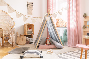 Cute pink little princess playroom in scandinavian design with peacock chair, pillows, carpets, toys and tent with toys, real photo