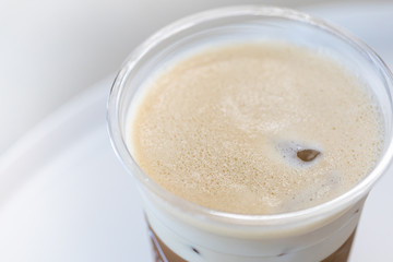 Close up of milk foam of iced coffee latte in take away plastic cup on white table.