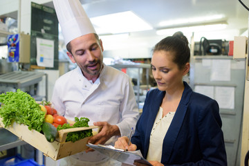 portrait of attractive cook and woman with clipboard in kitchen