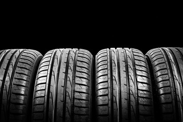 Studio shot of a set of summer car tires isolated on black background. Tire stack background. Car tyre protector close up. Black rubber tire. Brand new car tires. Close up tyre profile. Tires in a row