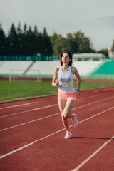 Young woman in pink shorts and tank to running during sunny morning on stadium track