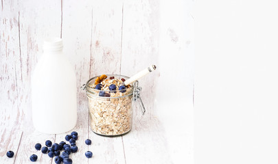 Muesli with blueberries in glass jar on white wooden background. 