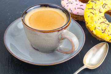 Cup of espresso with fresh pastries for breakfast on black stone background.