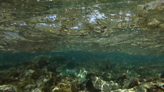Clear water of the sea with a rocky bottom. Waves in the sunshine