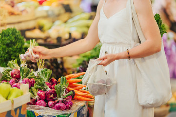 Young Woman puts fruits and vegetables in cotton produce bag at food market. Reusable eco bag for...