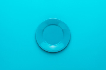 Top view photo of empty blue plate. Minimalist flat lay image of round ceramic plate over turquoise blue background with copy space and central composition. Mockup of blank dish on blue table.