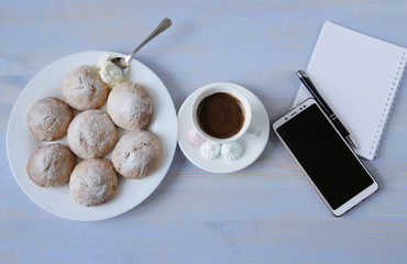 Top view of a workspace with a phone, a cup of coffee, cookies and a notebook with copy space on a light blue background. Flat lay. Home office workspace. 