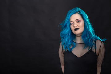 Style, fashion and hair concept - close-up portrait of young woman in black dress with blue hair on black background