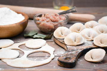 Raw dumplings on the cutting board and ingredients for their preparation: flour, egg, minced meat on a wooden table