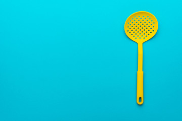 Top view photo of vivid plastic kitchen utensil. Minimalistic flat lay image of yellow skimmer spatula over turquoise blue background with copy space and right side position.