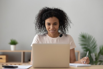 African woman student e learning making notes looking at laptop