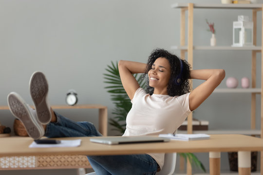 Relaxed African Woman Wear Headphones Listening To Music At Desk