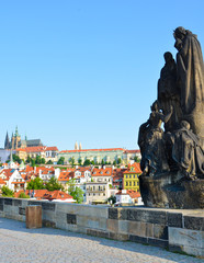 Sculptures on famous Charles Bridge in Prague, Czech Republic with blue sky. Prague Castle and other historical buildings in background. Popular tourist spot. Travel destination. Czechia, Europe