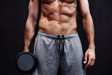 Close up of muscular bodybuilder guy doing exercises with weights over black background.