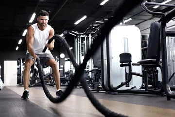 Gordijnen Atletische jonge man met slag touw doen oefening in functionele training fitness gym. © ty