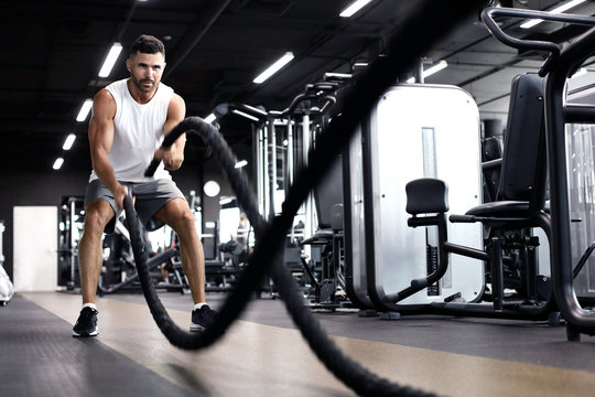 Athletic young man with battle rope doing exercise in functional training fitness gym.