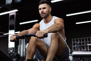 Fototapeta na wymiar Fit and muscular man using rowing machine at gym.