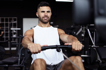 Fototapeta na wymiar Fit and muscular man using rowing machine at gym.