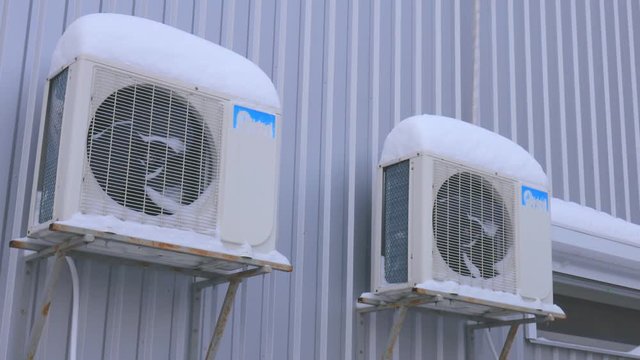 Outdoor air conditioner on the street in the snow. Fans are behind bars.
