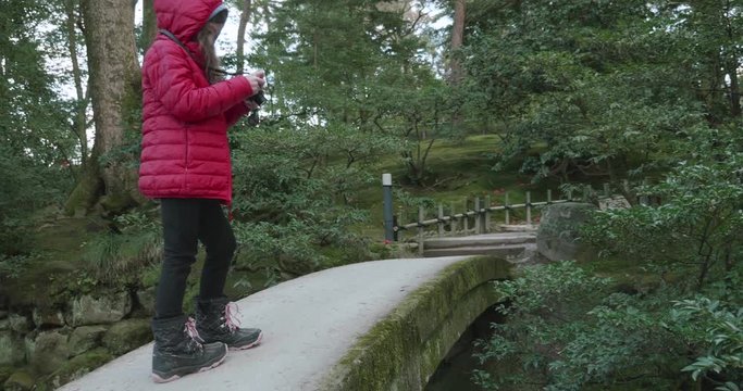 young girl photographing a stream from a concrete bridge in a Japanese park or garden checks the image then walks off the bridge
