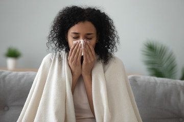 Ill african woman covered with blanket blowing nose got flu - obrazy, fototapety, plakaty