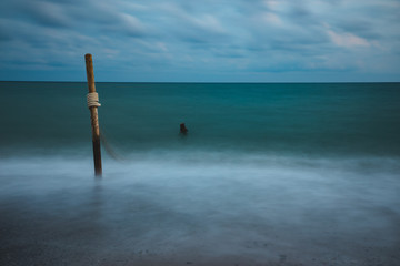 Long exposure of sea water with wooden logs and rope, on cloudy sky