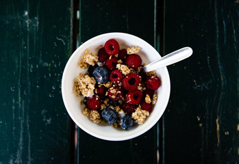 Muesli, wild berries and yogurt breakfast on white bowl top shot with black wooden background