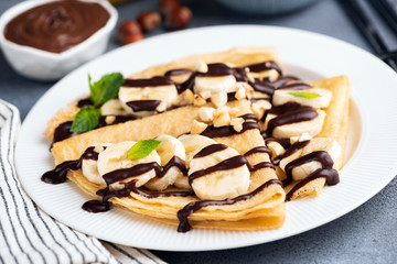 Crepe with banana and chocolate sauce on white plate, closeup view, selective focus. Tasty dessert