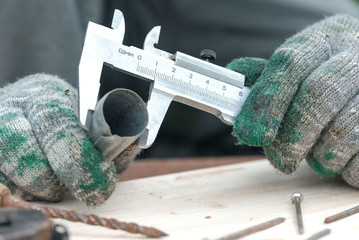 Worker is holding in hands a metal part and is measuring a diameter by a calipers.