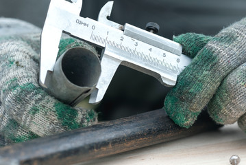Worker is holding in hands a metal part and is measuring a diameter by a calipers.
