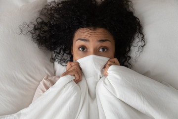 Surprised funny african girl in bed covering face with blanket