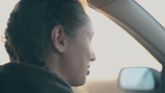 beautiful happy dark haired woman talks driving modern car at bright sunset light side view extreme closeup