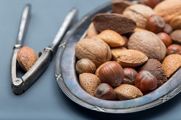 Different kinds of nuts in shell, hazelnut, walnut, almond and brazil nuts on  plate with nut cracker, horizontal