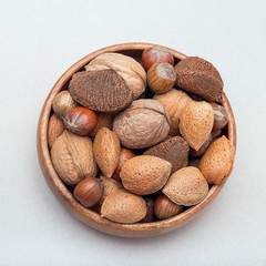 Different kinds of nuts in shell, hazelnut, walnut, almond and brazil nuts in a wooden bowl, square format, top view