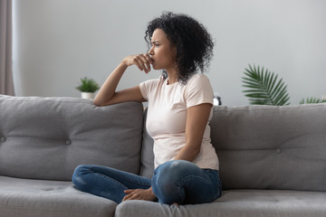 Sad thoughtful african girl on sofa looking away feel depressed