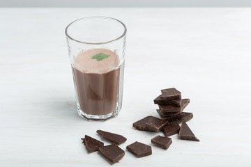 Glass mug with a protein chocolate shake stands against the background of a packet of protein on a white table. Sports nutrition concept.