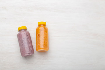 Two bottles with orange and blueberry juice lie on a white table. The concept of proper nutrition and a healthy snack at work. Copy space