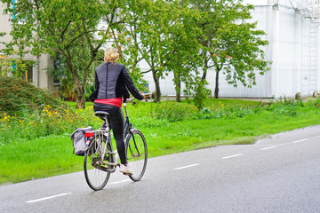 Woman riding a bike in the countryside of the Netherlands. The girl is riding her bike on the way to a Dutch village.