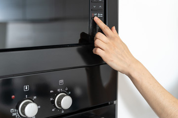 Woman holding hand on black microwave button