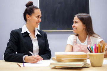 The teacher and the student sit in the classroom at school looking at each other and smiling