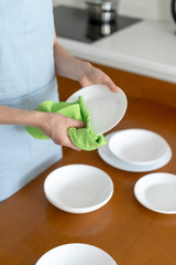 Woman cleaning plates and bowls on kitchen with wooden table