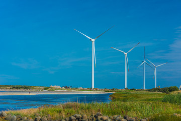 Four wind turbines by a bay and a small beach.